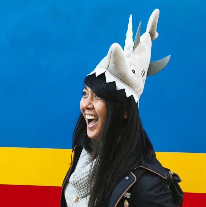 Charlyn smiling facing the left with a light up shark hat in front of a blue, yellow, and red background.