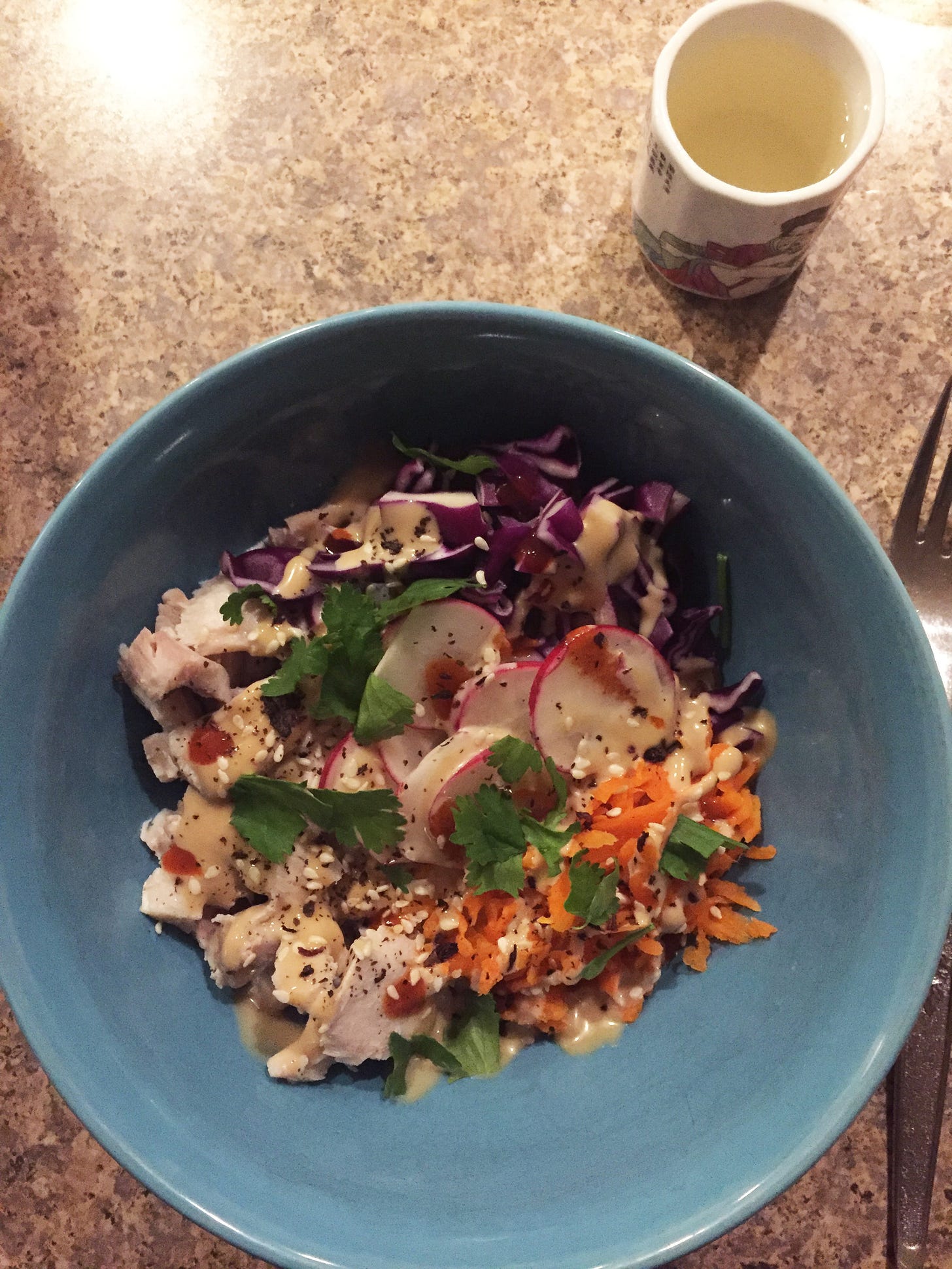 A blue bowl of rice and salmon flakes with little piles of shredded carrot and cabbage, and sliced radish. Teriyaki mayo and hot sauce are drizzled over top, along with cilantro, sesame seeds, and shiso furikake.