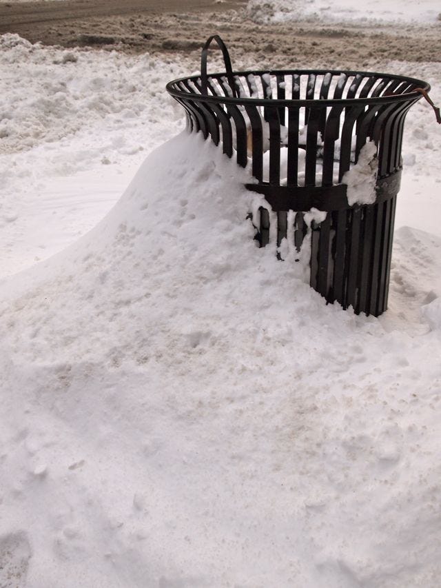 snow piled high against a city garbage bin