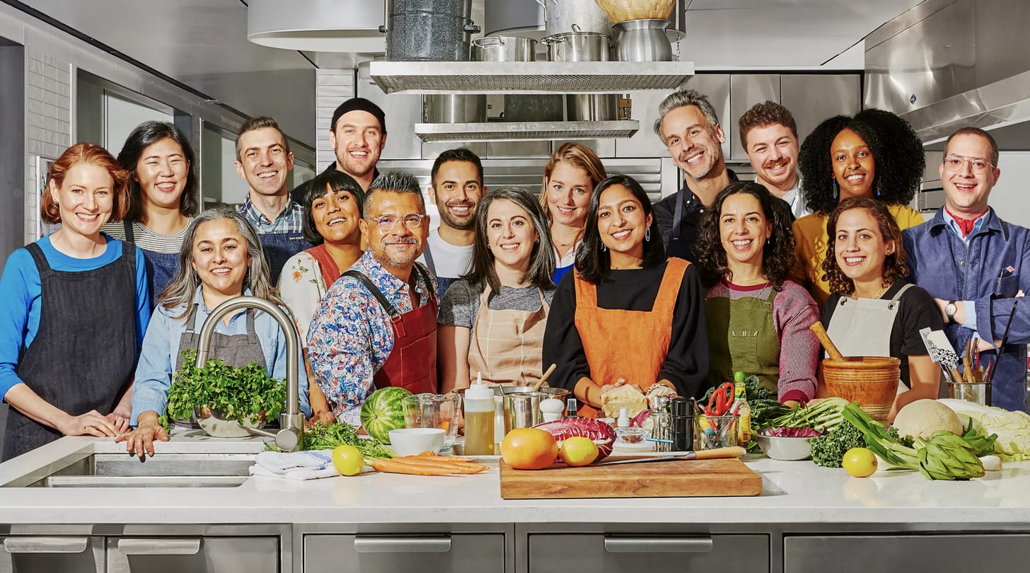 Studio lighting photo of Bon Appetit’s YouTube Staff smiling in the kitchen with food on the counter.
