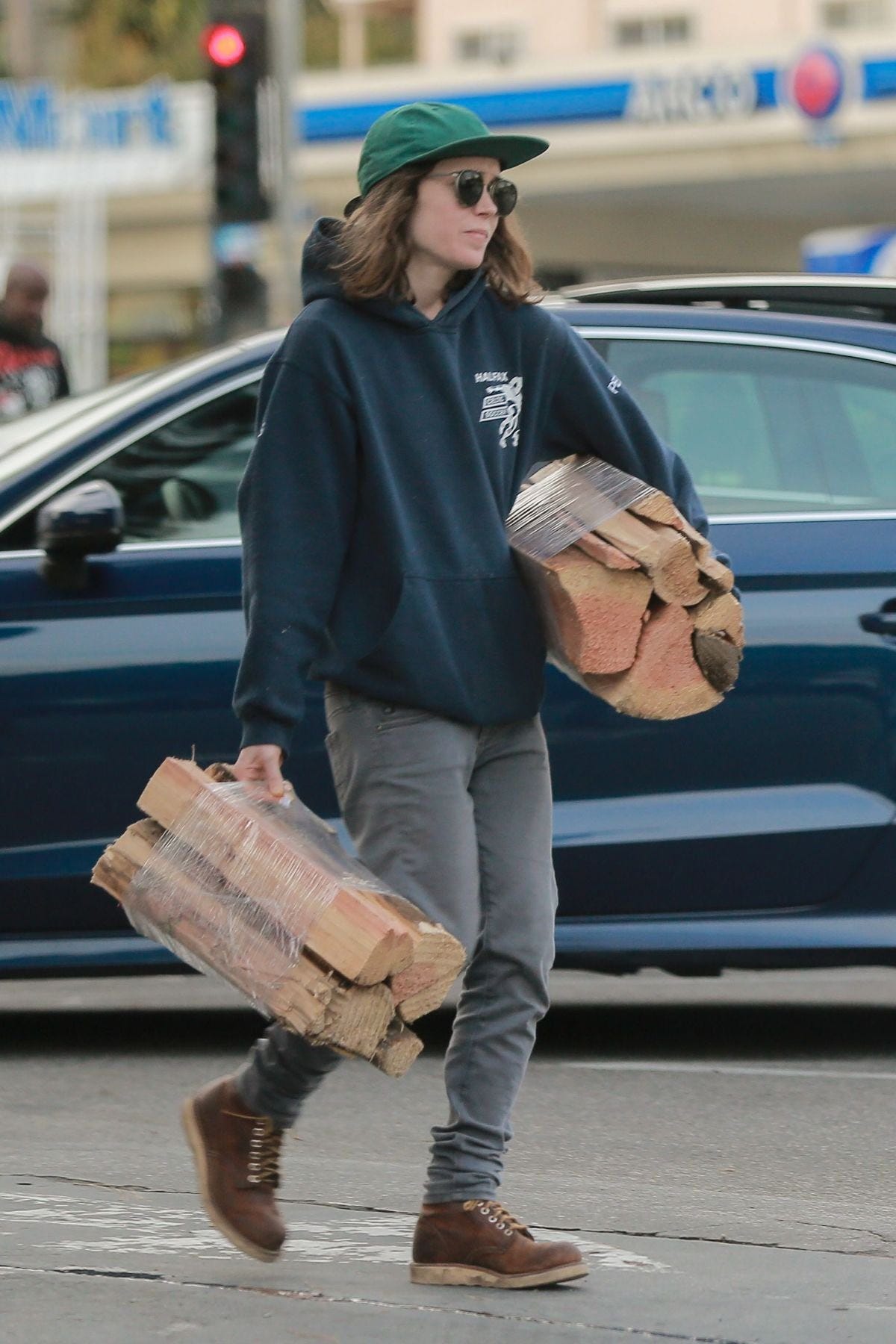 Elliot Page in a candid shot, looking unbothered and carrying two stacks of firewood in each arm