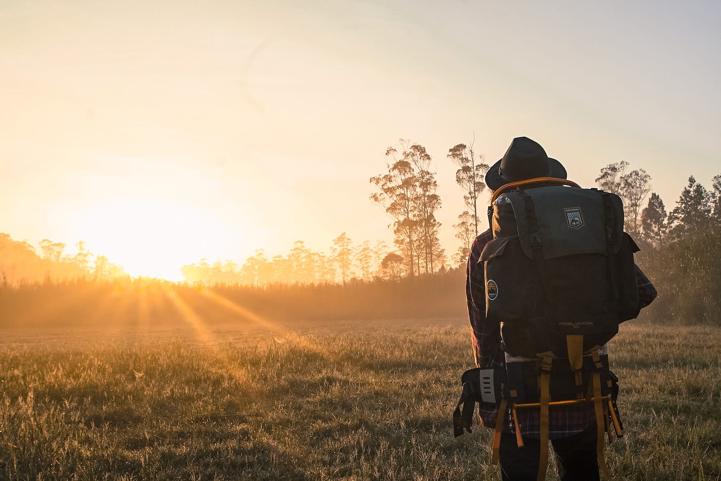 man in hiking gear looking at sunset standing in field
