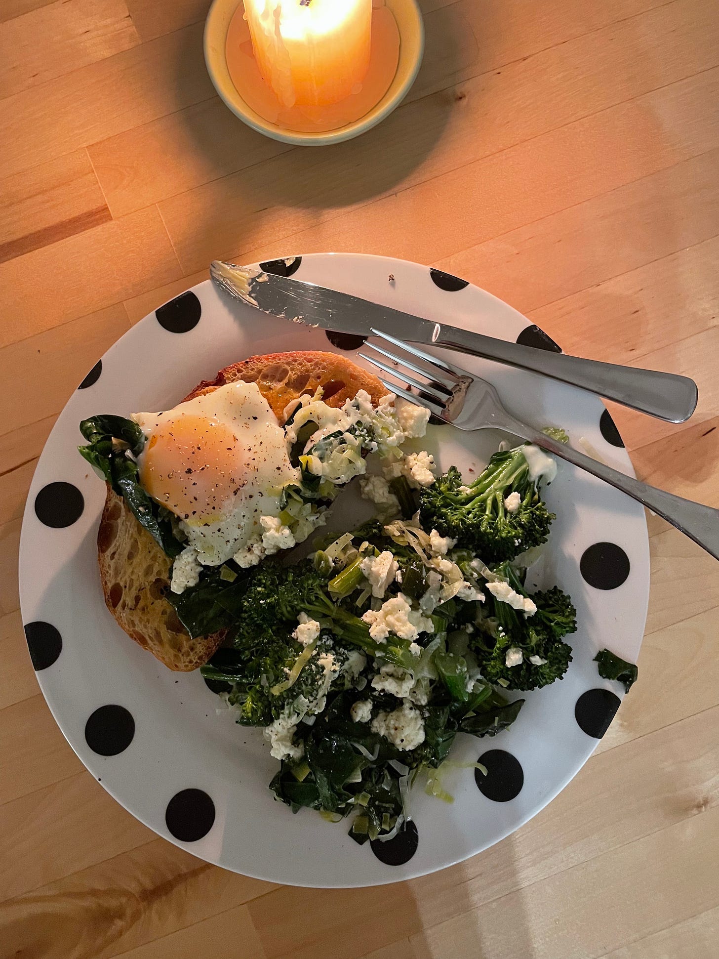 Buttered toast on a spotty place topped with a baked egg and braised green veggies and feta cheese.