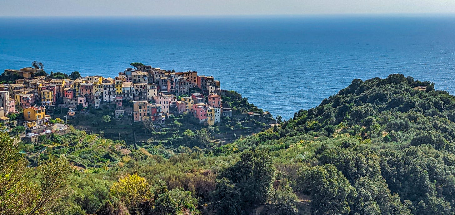 Corniglia in the distance, the ocean behind it, a green hill in front. 
