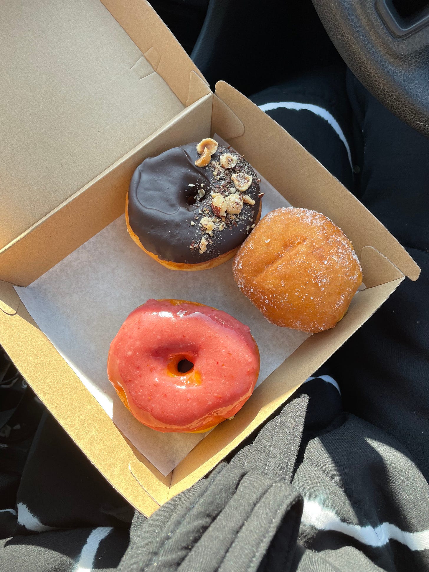 Box of two iced doughnuts and one jam doughnut on a lap in a car