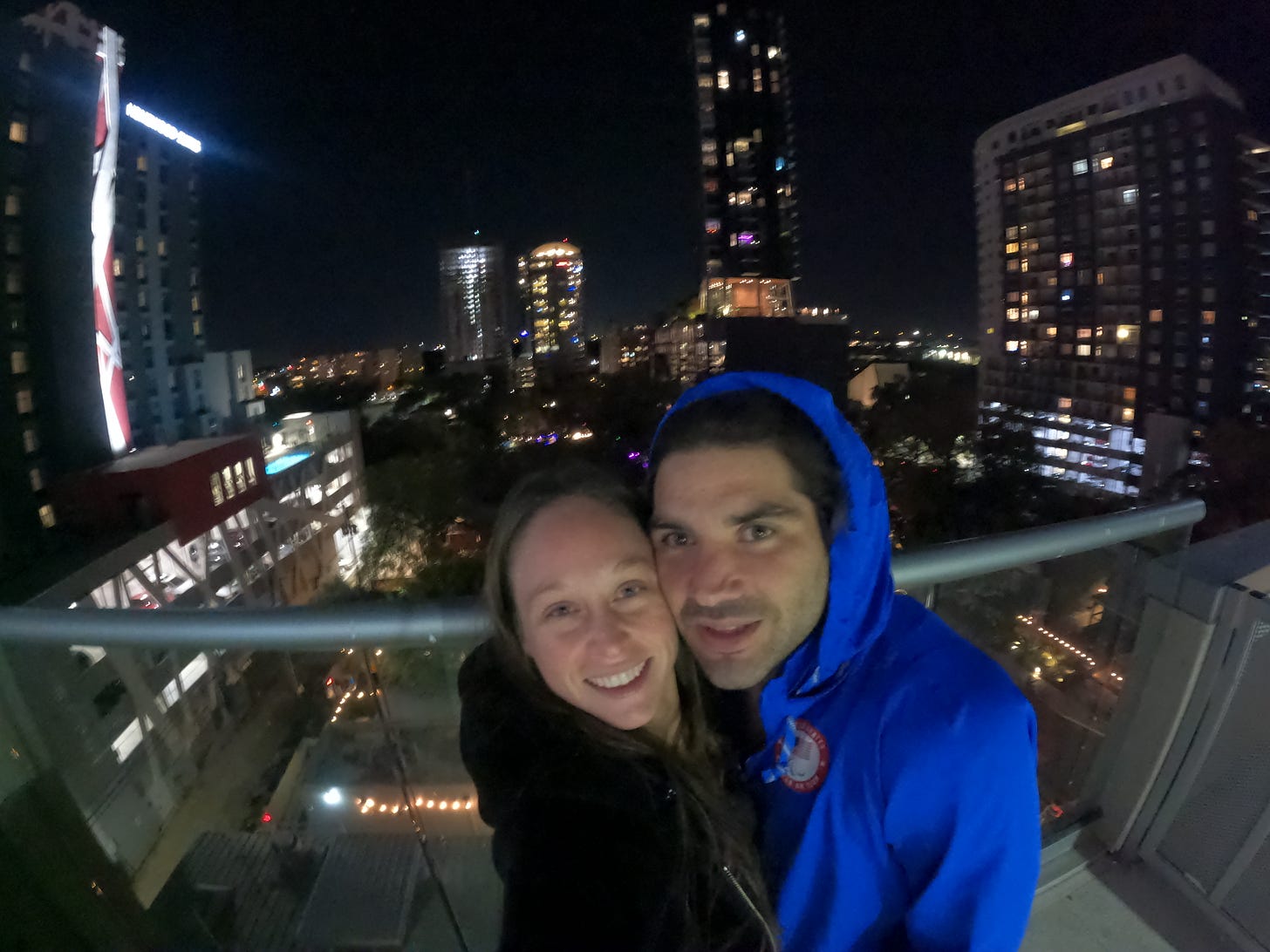 Anthony and kelly stand on the roof top at night overlooking downtown austin