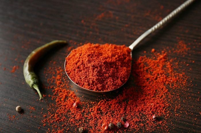 A photo of a tablespoon of paprika on a table next to a chili pepper