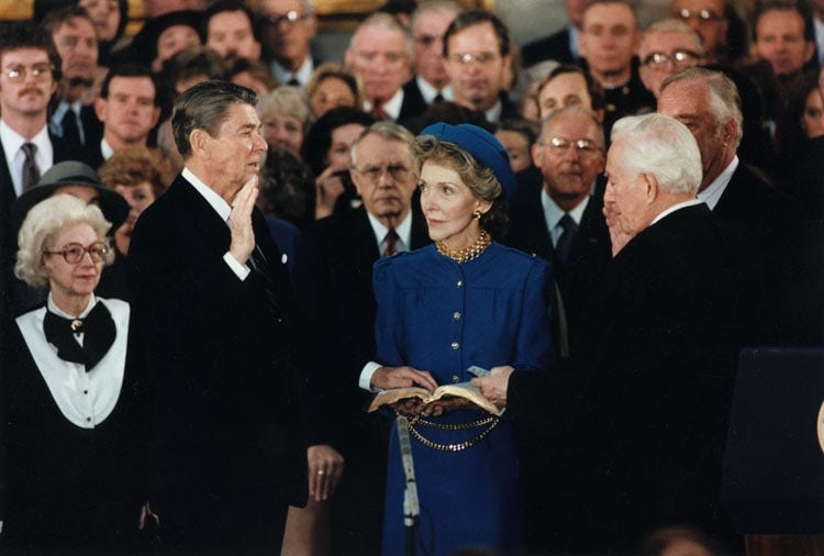 Ronald Reagan is sworn in for the second time. Nancy Reagan stands next to her husband, holding a Bible while he takes his oath.