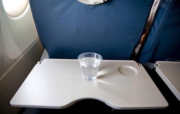A tray table with a beverage located precariously outside the beverage bunker.