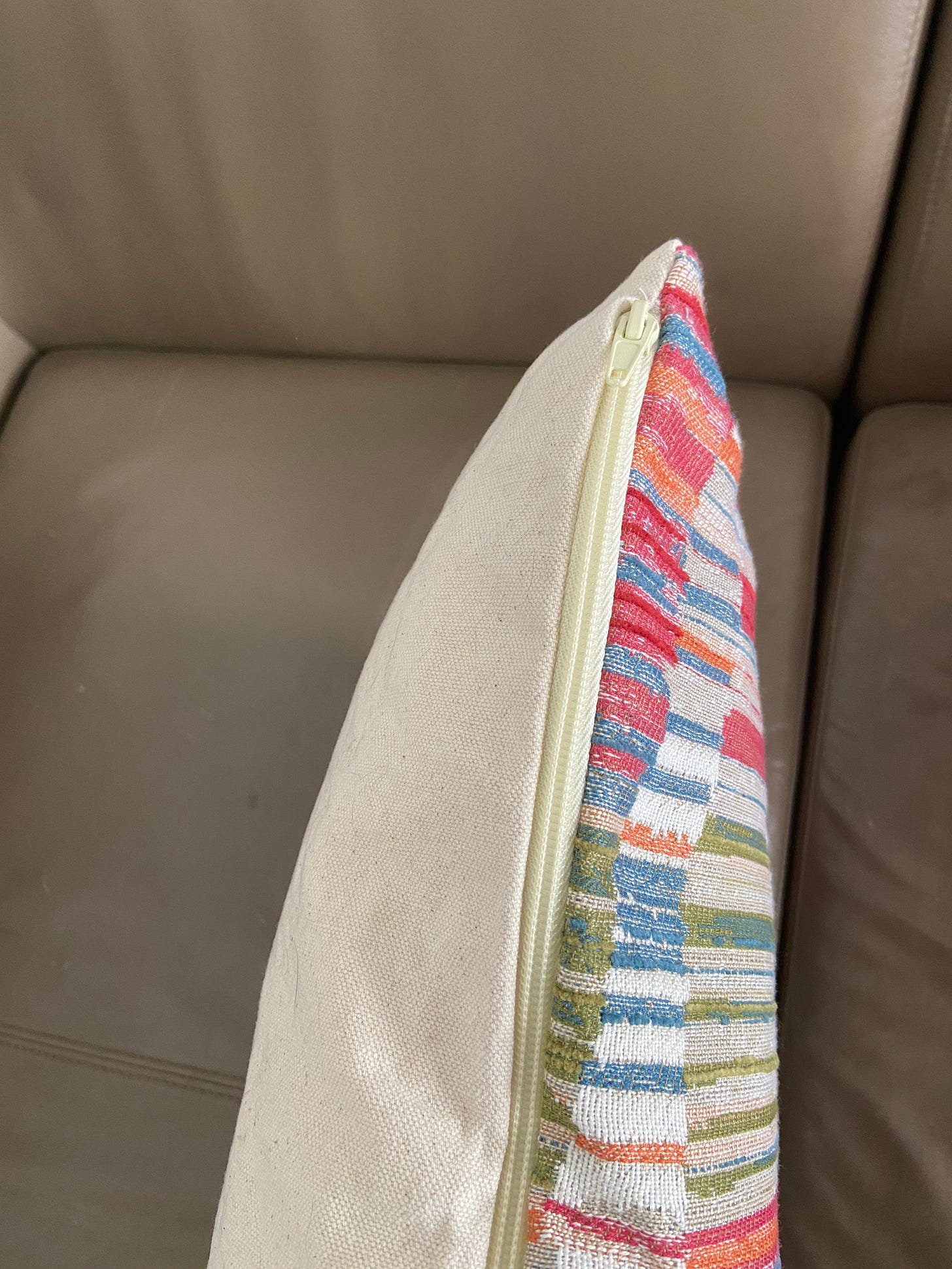 A side view of the pillow, showing the patterned face and the canvas backing, bisected by an off white zipper.