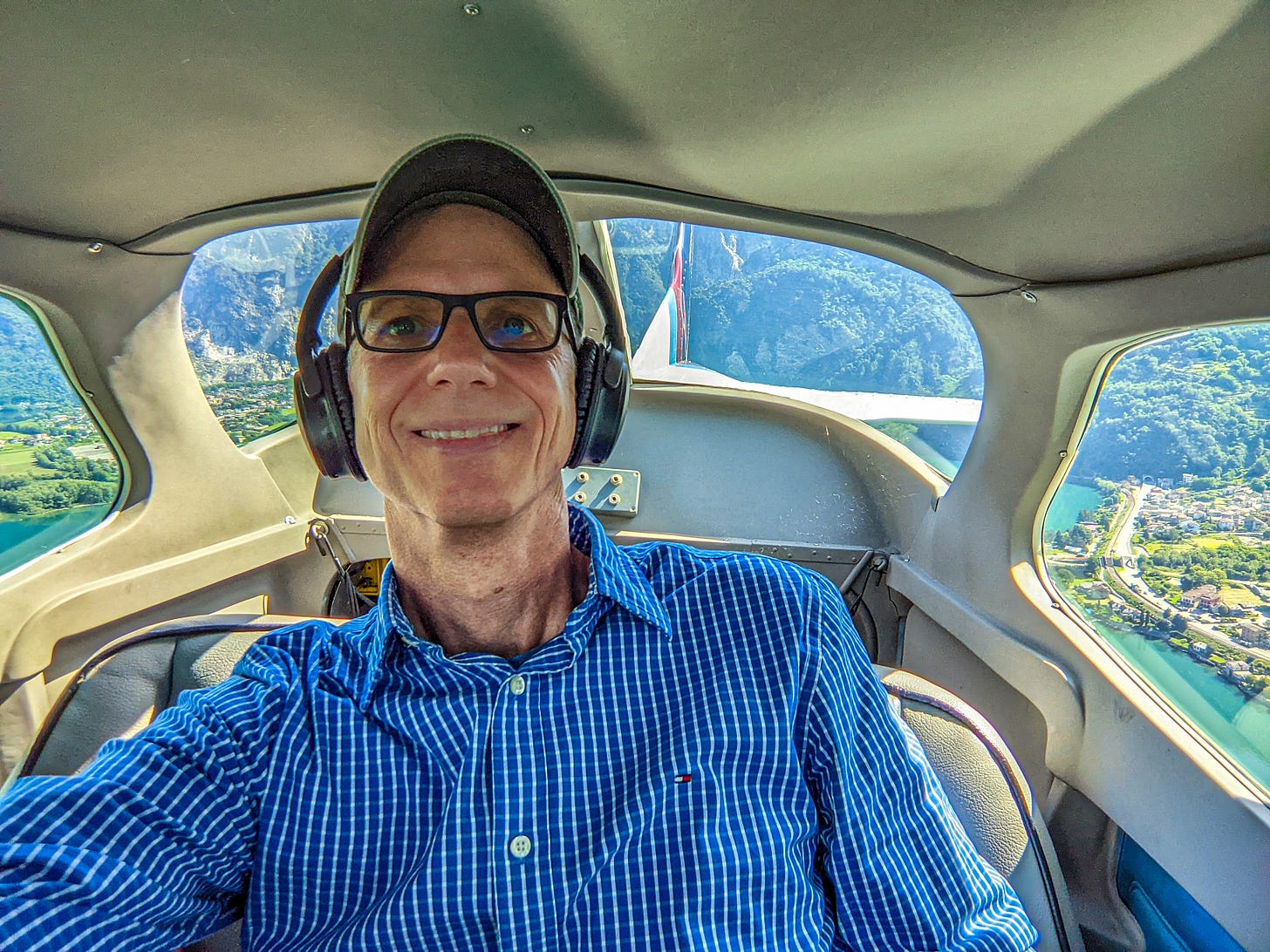 A selfie of Michael sitting in the back of the plane, the lake and mountains visible behind him. 