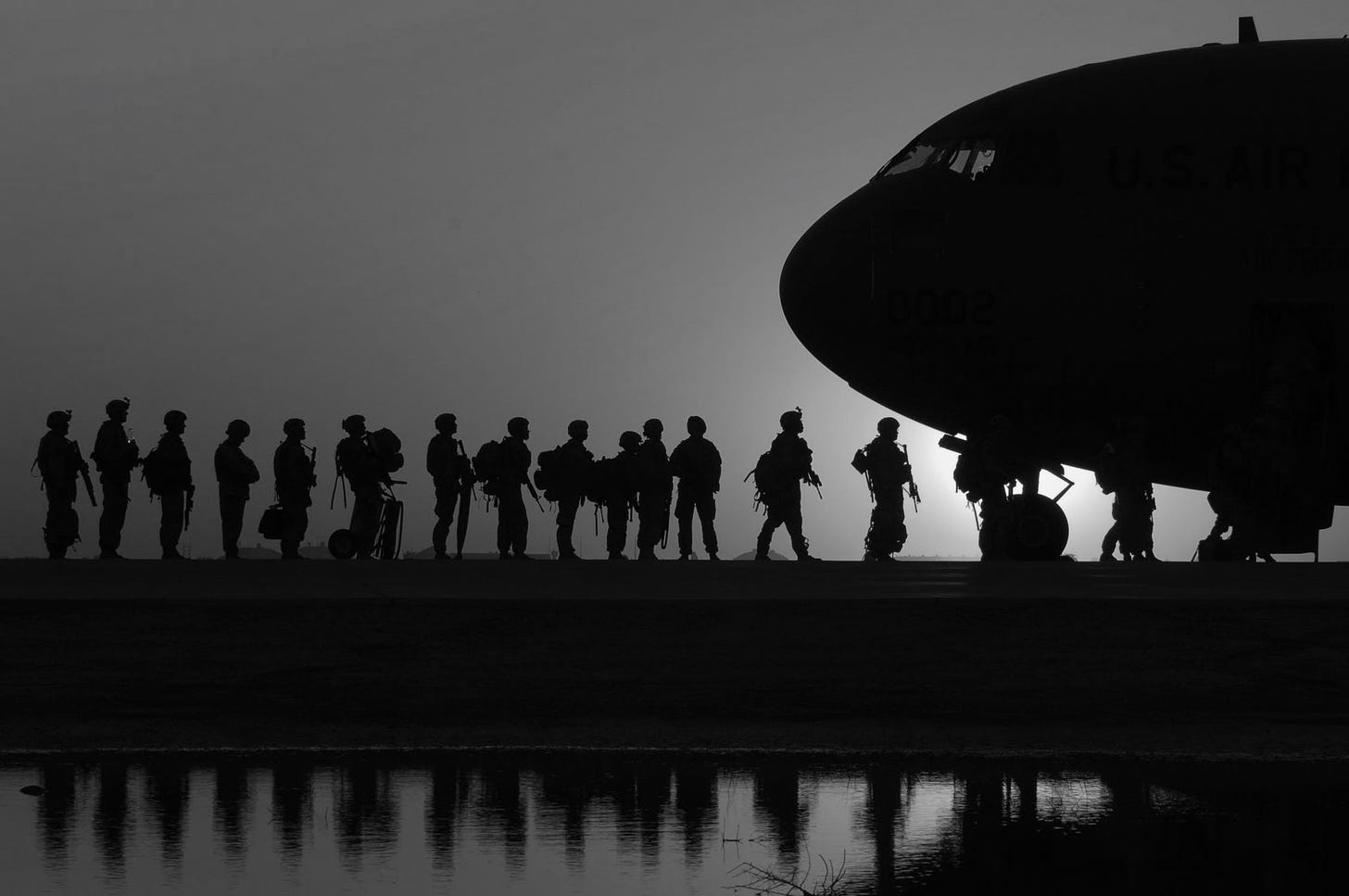 At dusk or dawn, the silhouettes of soldiers lined up to board a jet