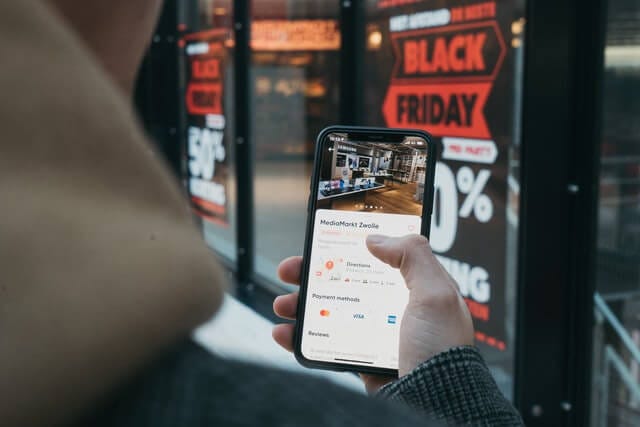 person holding phone in front of black friday sign