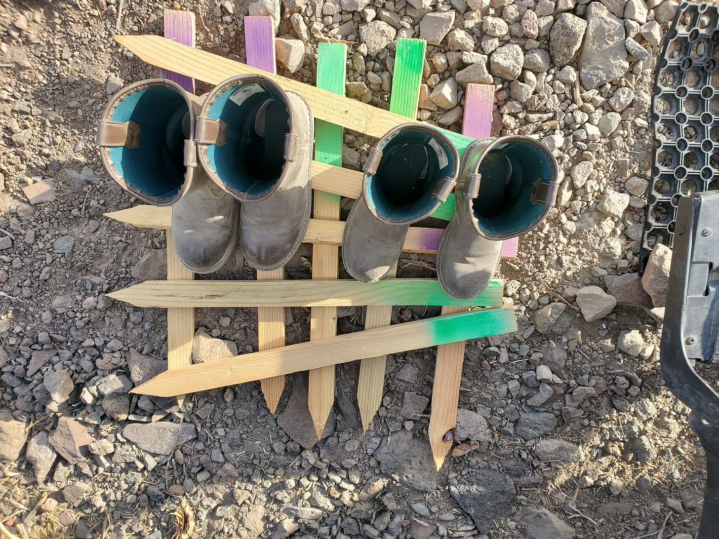 Two sets of dusty children's work boots on crisscrossed wooden stakes on the ground.