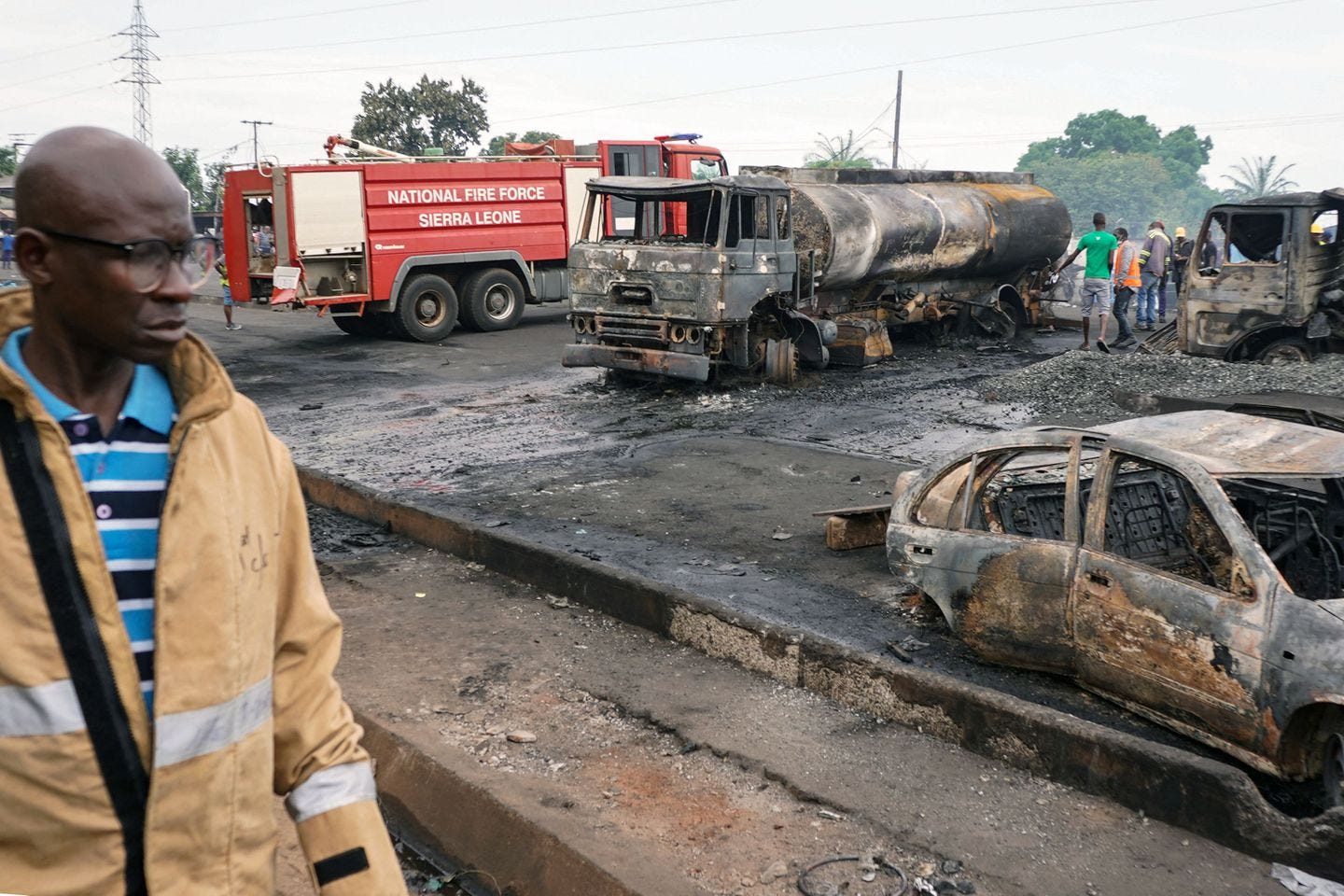 A man walked past burned vehicles in Freetown on Saturday, following a massive explosion that killed more than 90 people.