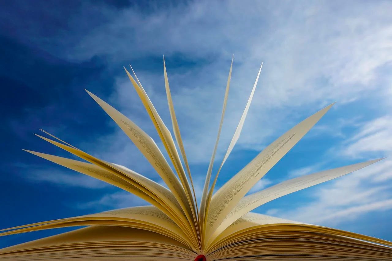 side view of open book with flipped pages in front of blue sky with clouds