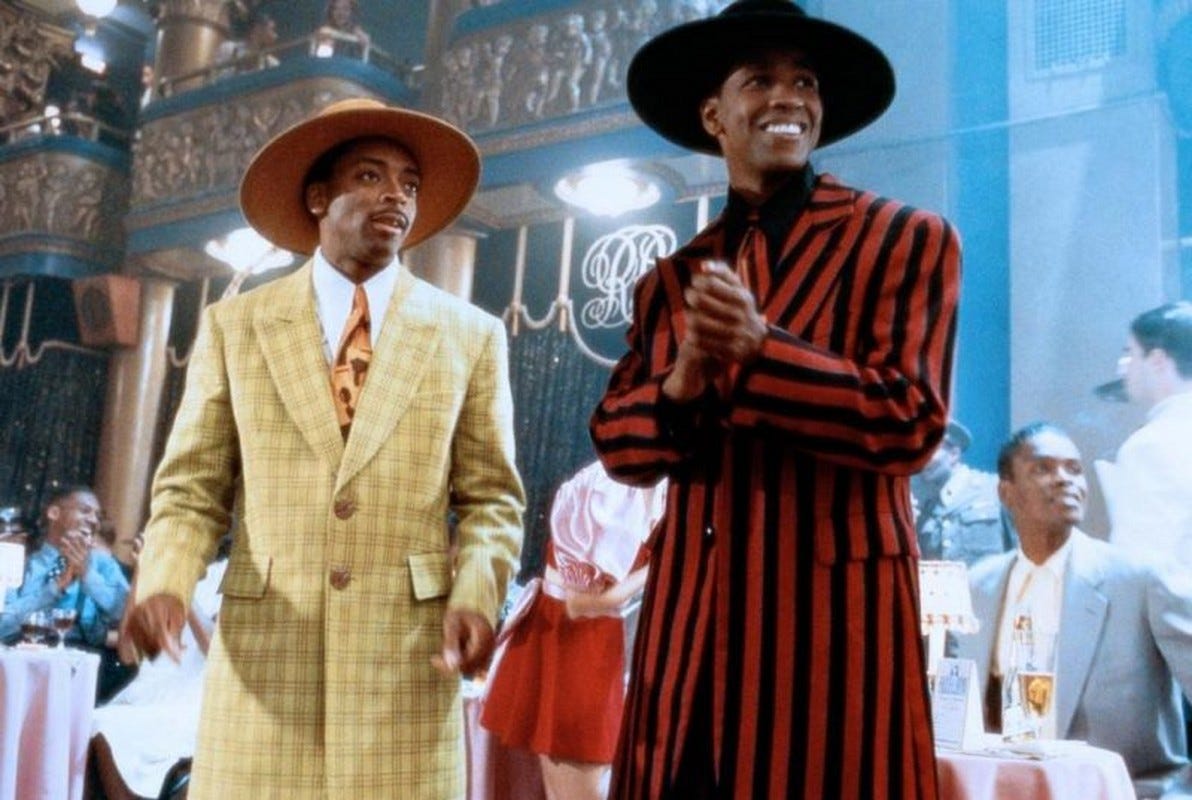 This image shows the characters of Shorty (played by Spike Lee, left) and Malcolm Little (played by Denzel Washington, right) dressed in colorful zoot suits. Both men, standing in Boston, Massachusetts's Roseland Ballroom, look to their left. This image shows the characters of Shorty (played by Spike Lee, left) and Malcolm Little (played by Denzel Washington, right) dressed in colorful zoot suits. Both men, standing in Boston, Massachusetts's Roseland Ballroom, look to their left.