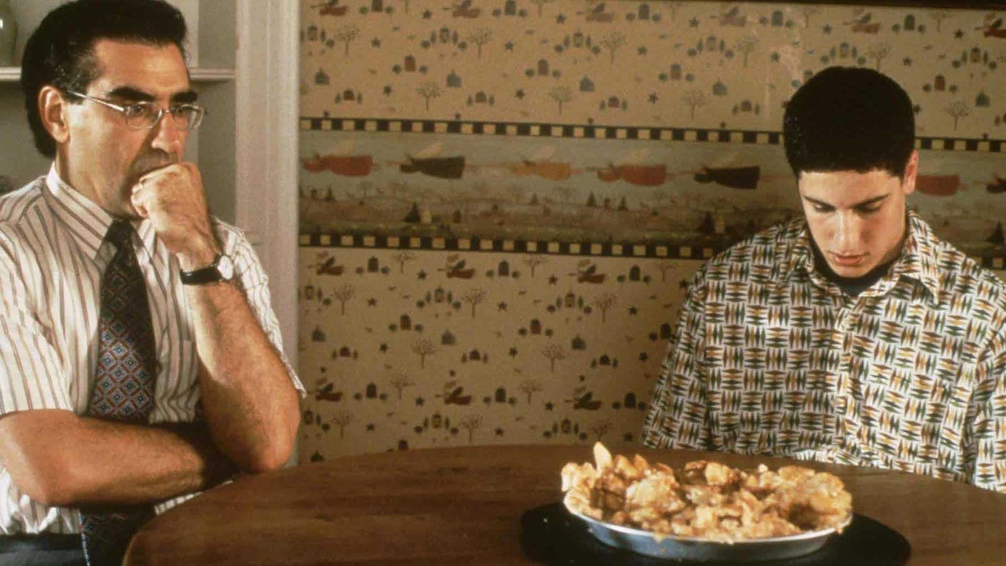 Movie still from American Pie. A teenage boy sits dejectedly at the table with his dad, looking down in shame at a pie.