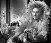 Miss Havisham from the 1946 black and white film Great Expectations. Old lady dressed in an old bridal gown sat in a dust covered room.