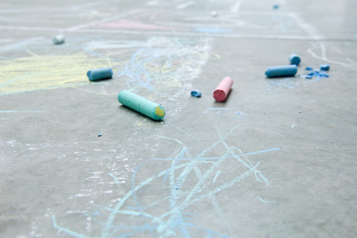 Multicolored sidewalk chalk scattered on an asphalt surface with some scribbles