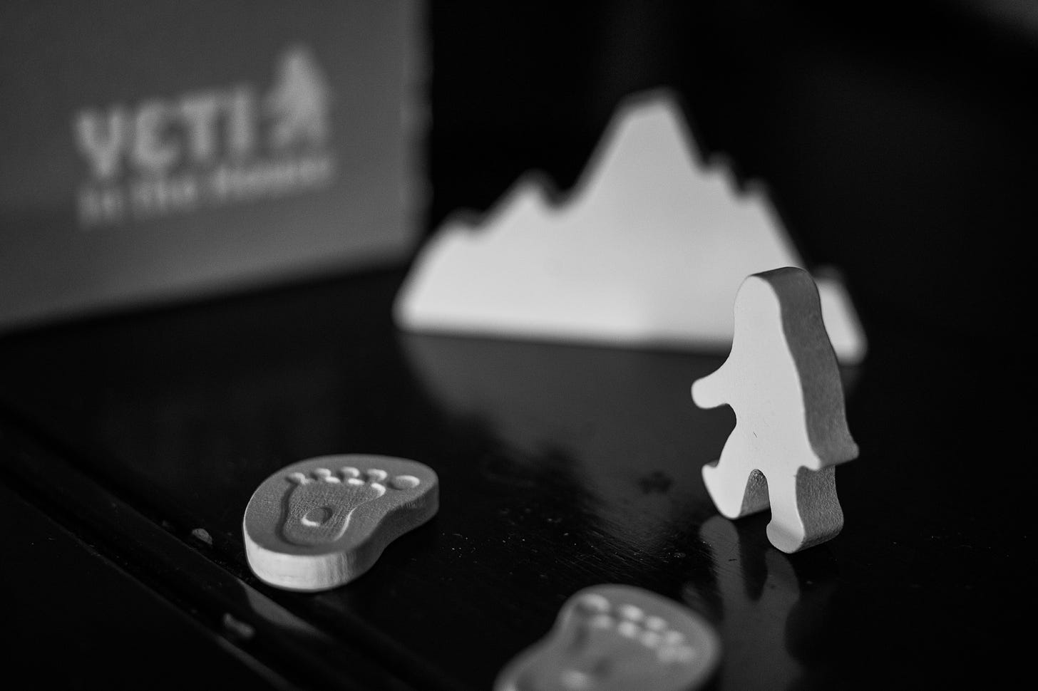The board game Yeti in the House on a table. Components from the game are visible, including a yeti token, two footprint tokens, and a larger mountain token.