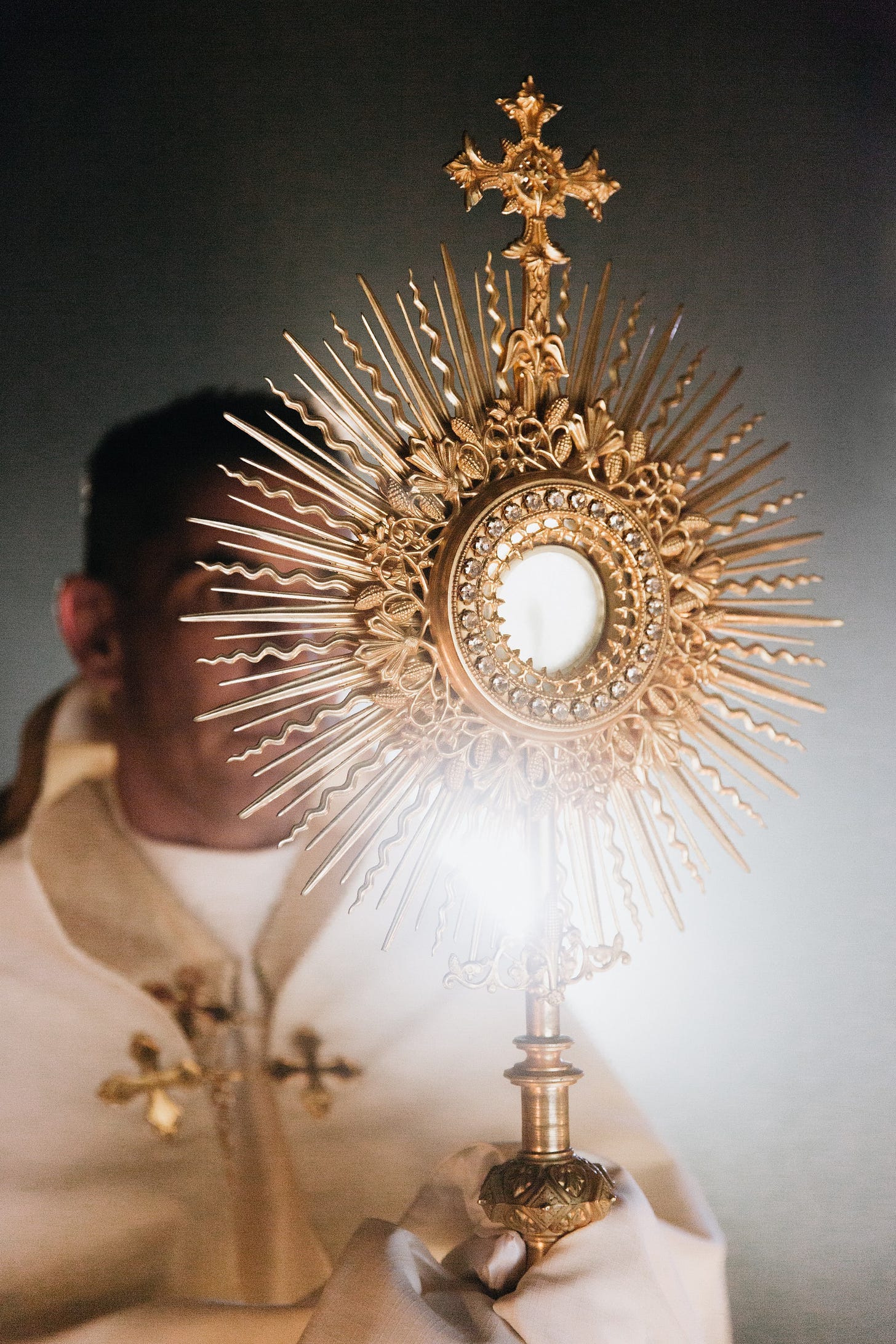 Image of a priest holding up a monstrance in which a consecrated host is displayed in a sunburst of rays