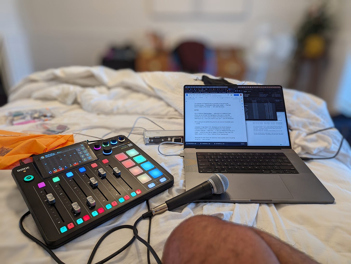 laptop and rodecaster and microphone sit on messy unmade bed