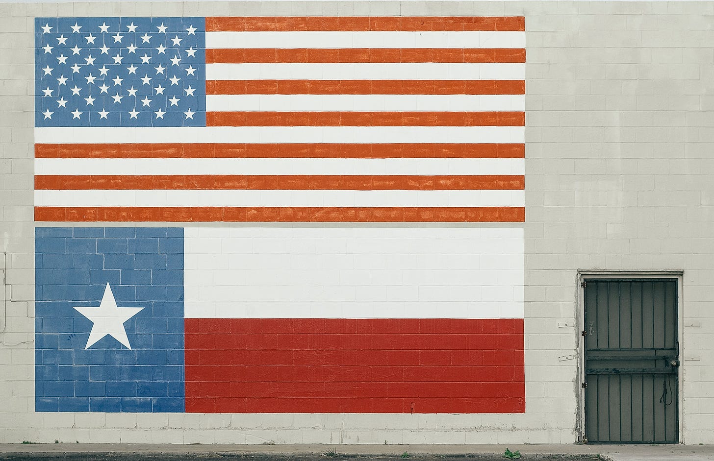 A mural of the American flag above a mural of the Texas flag, both pointed on the exterior of a white brick building. Matthew T. Rader / Unsplash