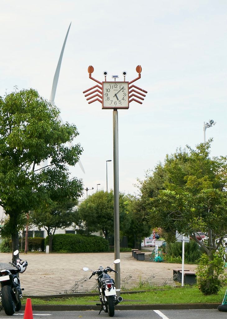A clock on top of a tall pole that looks like an adorable lil crab guy.