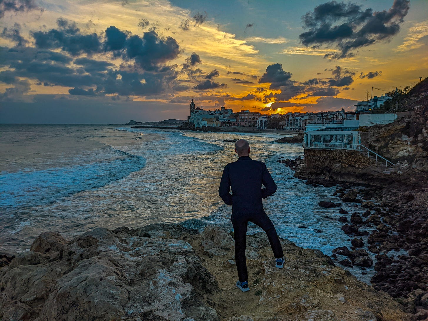 Brent standing on a rock overlooking the rocky coast up toward Sitges with a golden sunset providing the perfect backdrop.