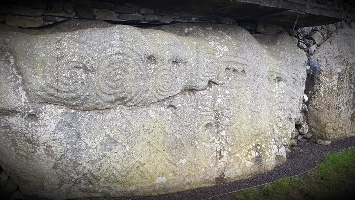 Large grey kerbstone at Newgrange with various markings including circular concentric motifs, rows of lozenge designs