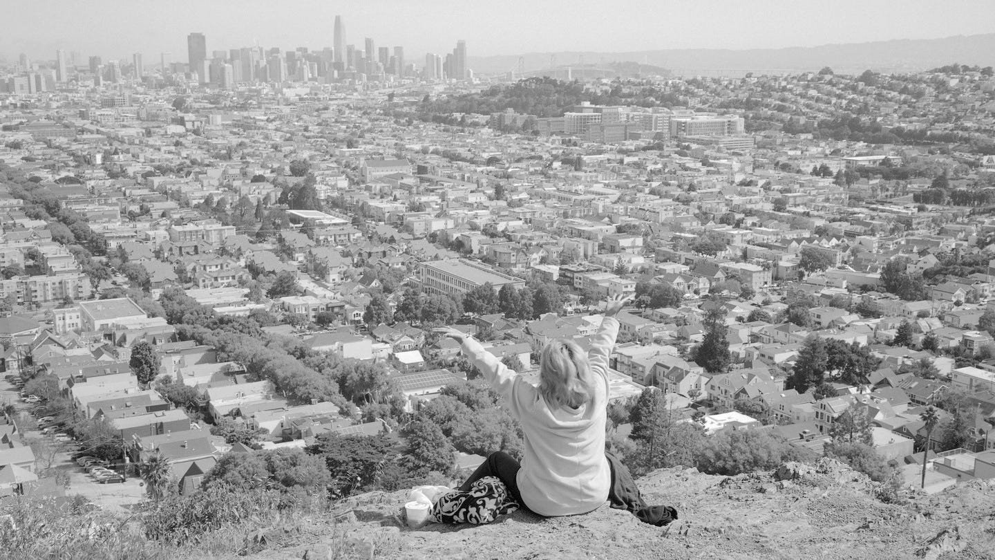 A black-and-white image of a  woman raising her hands overlooking the city of San Francisco