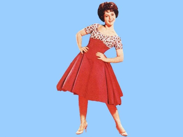 Sandra Lee, a petite white woman with short brunette hair, in a promotional photo with a full red skirt and patterned top. She has her hands on her hips and is smiling.