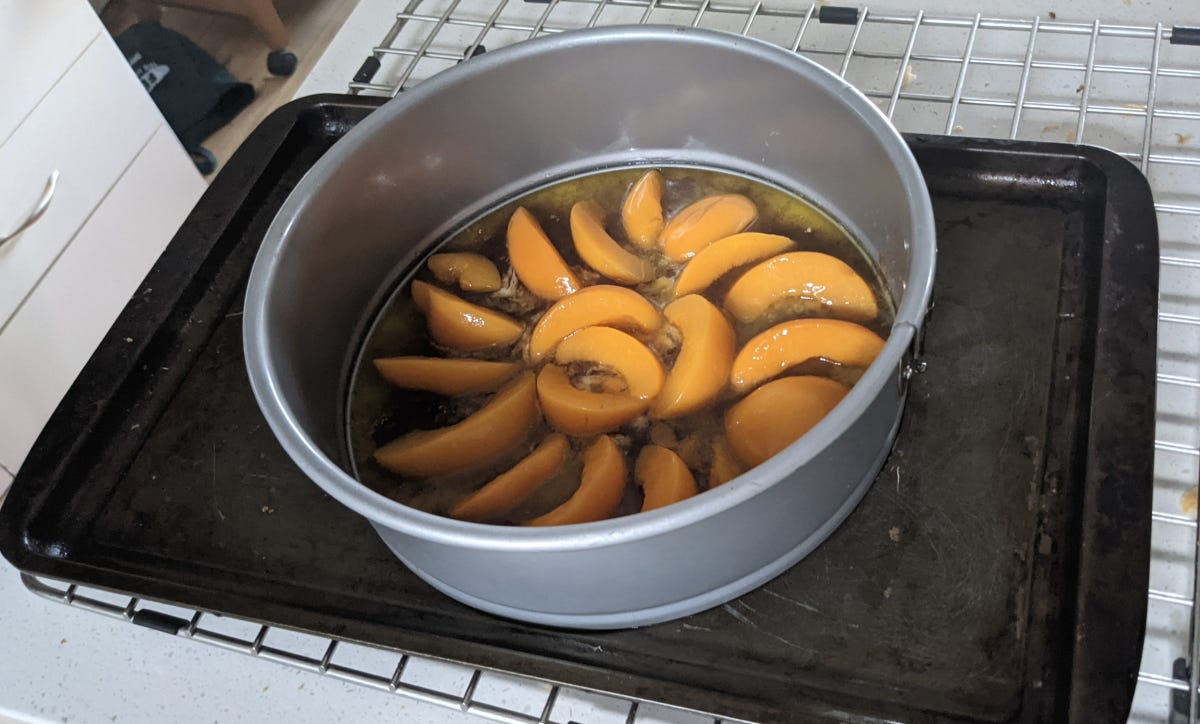 Peaches in glaze slowly seeping out of a spring-form tin into a baking tray