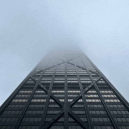 A stop-motion photo animation loop looking up at the John Hancock building in Chicago, the top covered by fog. The camera starts low and then moves straight up so it is only looking at fog. 