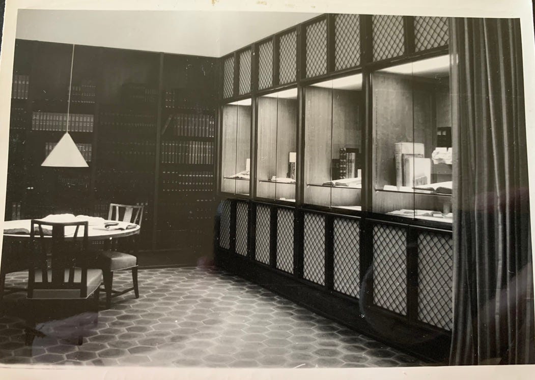 Black and white photo showing lit display cases and library bookshelves.