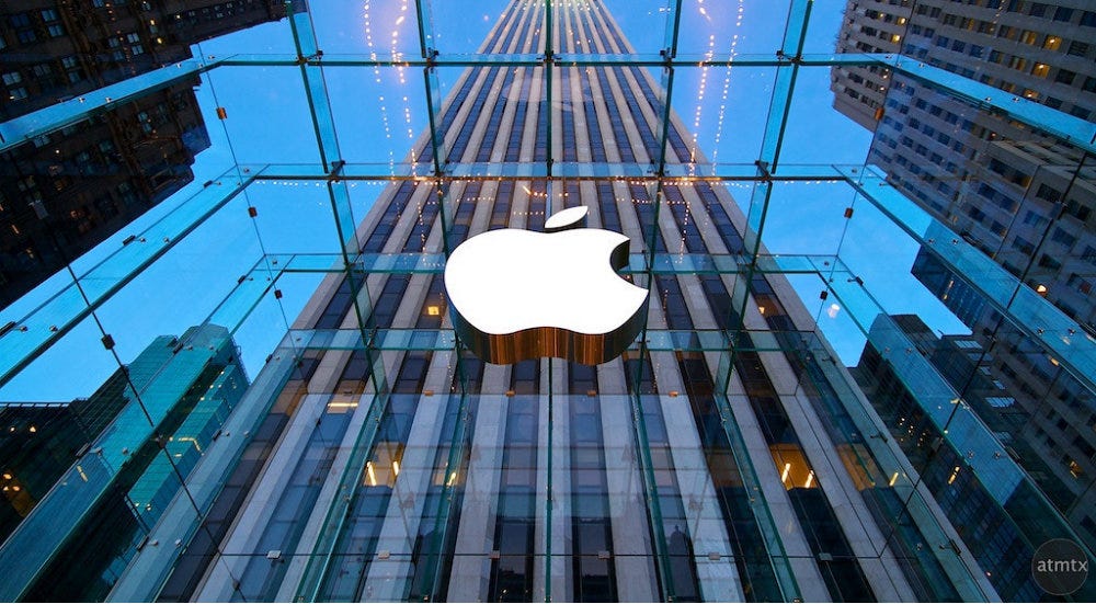 The gleaming exterior of an Apple store, with skyscrapers reflected in its glass windows.