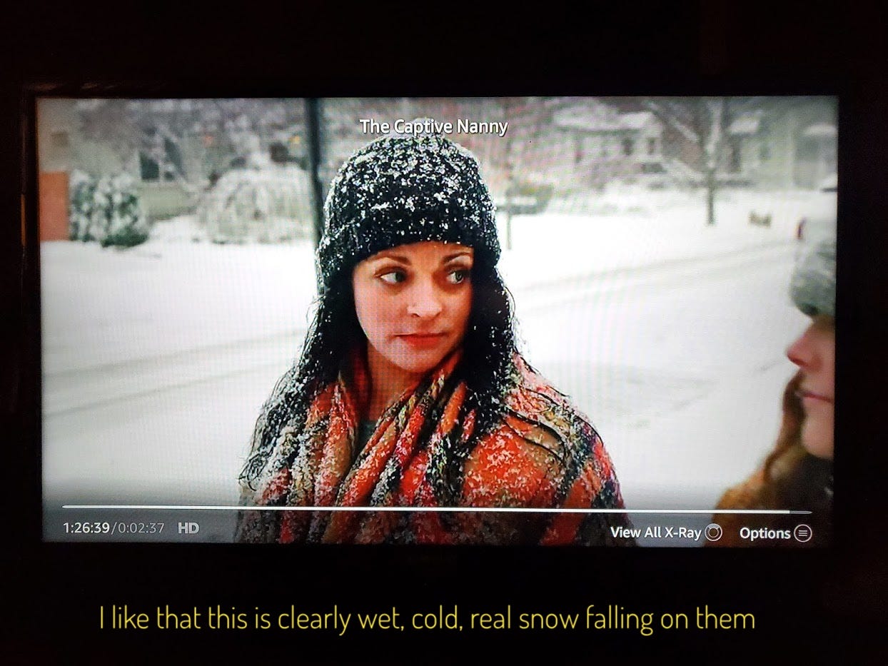 Stephanie in a blanket coat and knit hat, covered in snow, captioned "I like that this is clearly wet, cold, real snow falling on them"