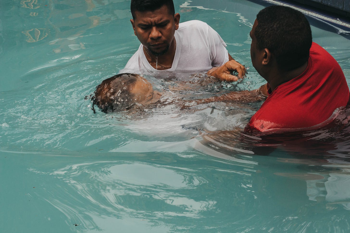 A person being baptized in a pool by two men.