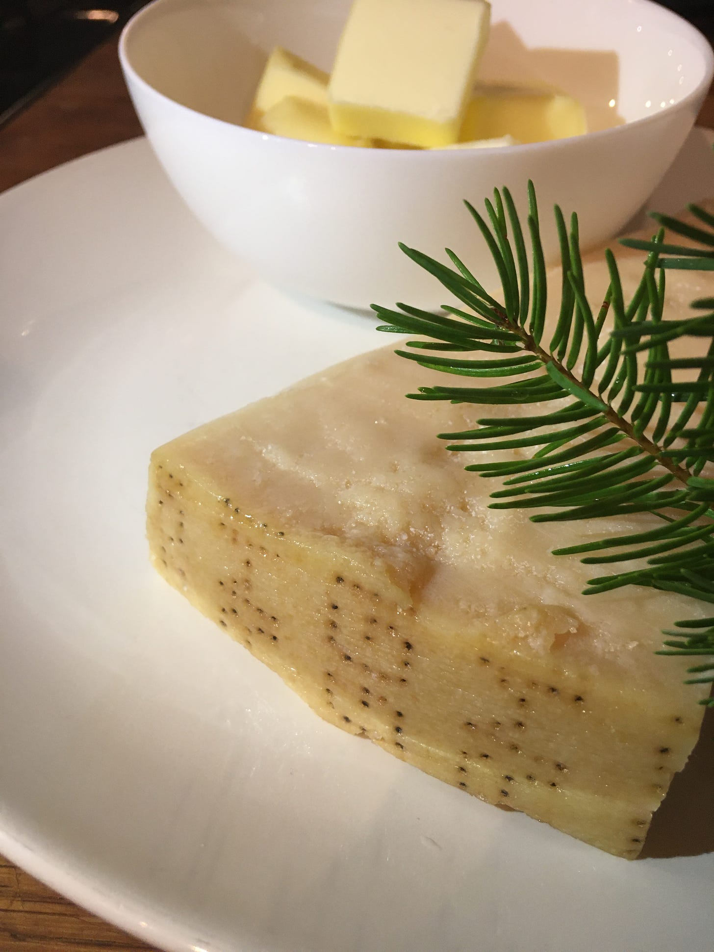 A mise en place with a white plate holding Parmigiano-Reggiano and a sprig of Douglas Fir. A white bowl holding cubed butter to make fettucine alfredo.