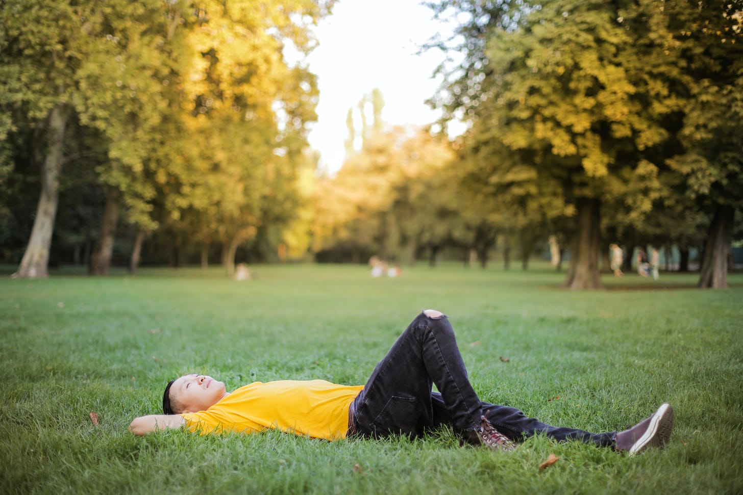 A man in a yellow shirt lying in a grassy field looking up at the sky.
