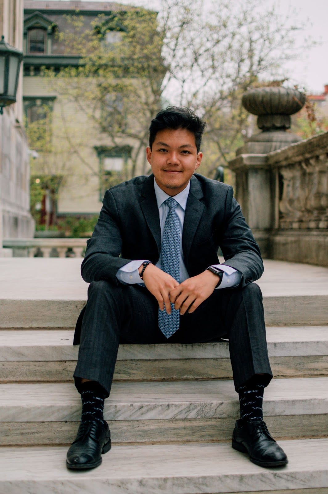 Ivan Zhao is pictured wearing a suit and tie, and sitting on some stone steps