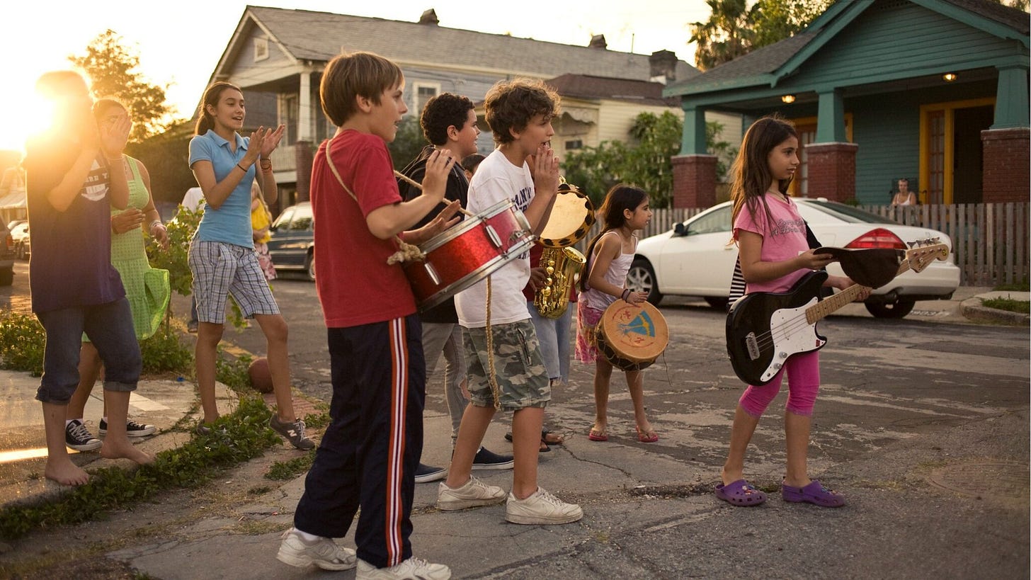 A group of children hold jazz instruments and sing in a neighborhood street.