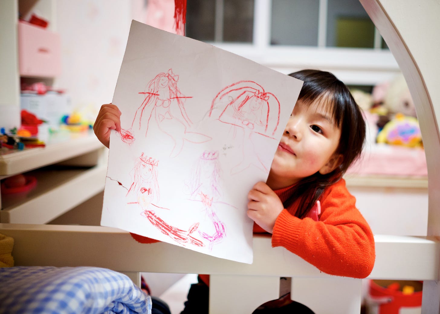preschool asian girl holding up a crayon drawing of a mermaid