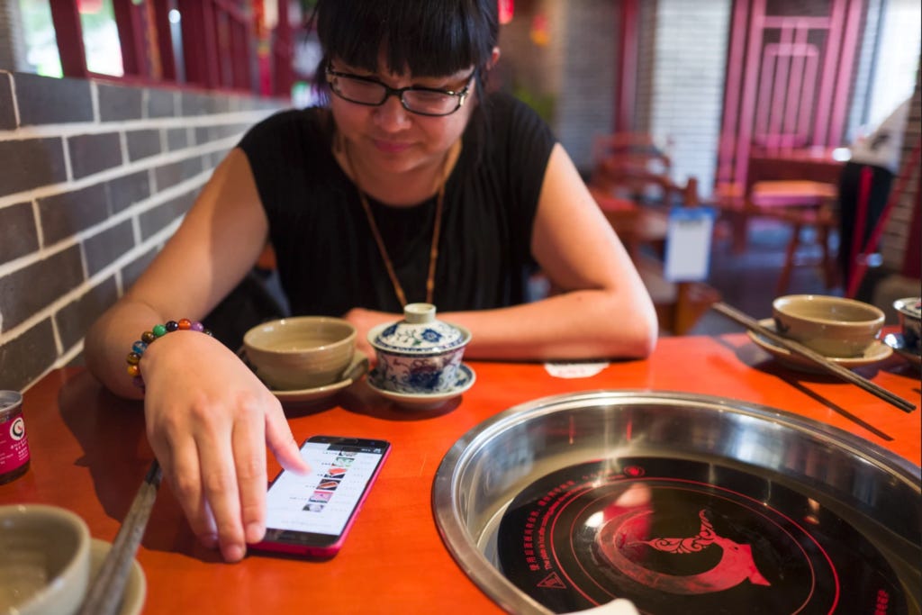 An Xiao Mina sitting at a hot pot table and scrolling through a phone