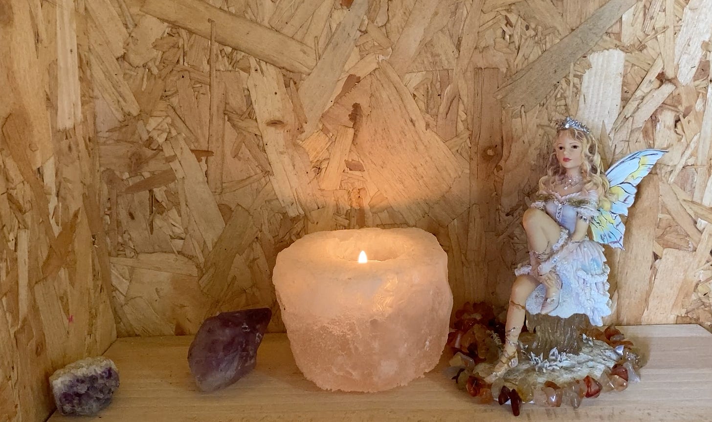 shelf with 2 purple amethysts, a seated fairy and a light candle in a salt holder