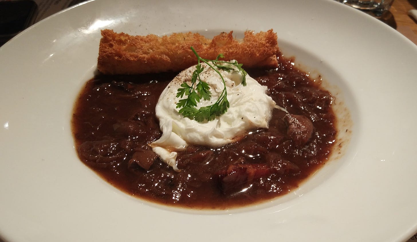 Oeuf en meurette, a french starter dish consisting of a poached egg in a bed of rich, reddish beef bourgignon sauce and a piece of crispy bread. Garnished with a sprig of parsley.