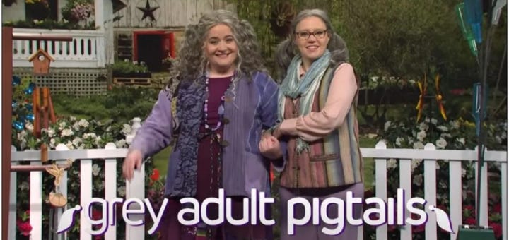 Aidy Bryant and Kate McKinnon wearing grey adult pigtails