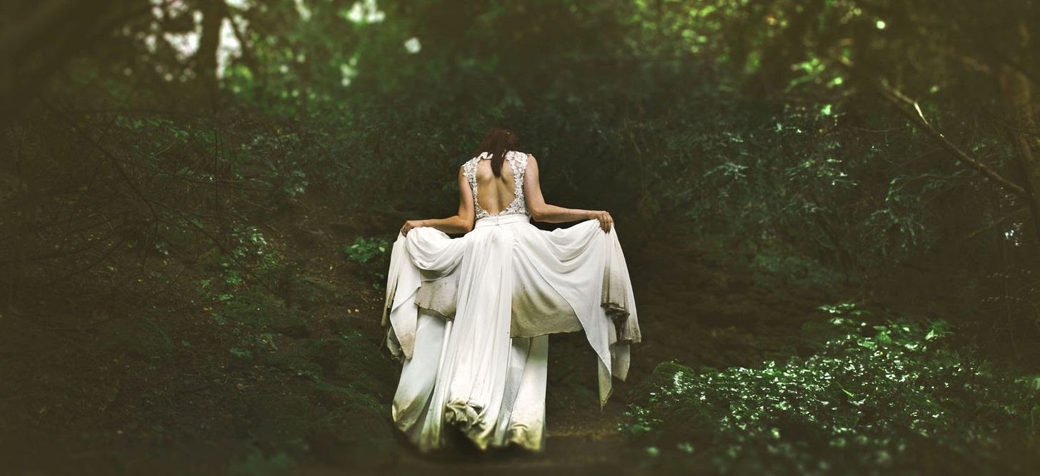 a woman in what is probably a white wedding dress walking into the forest