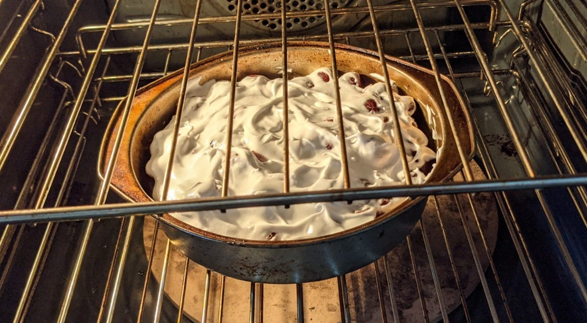 A baking dish containing some cherries covered in undercooked meringue